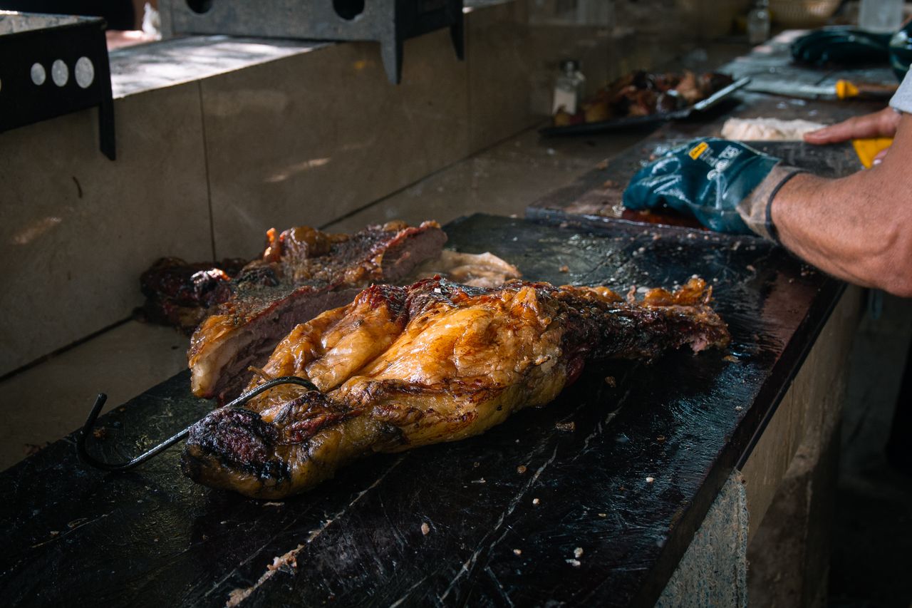 Delicious barbecue meat on a rustic cutting board with chef preparing at grill.
