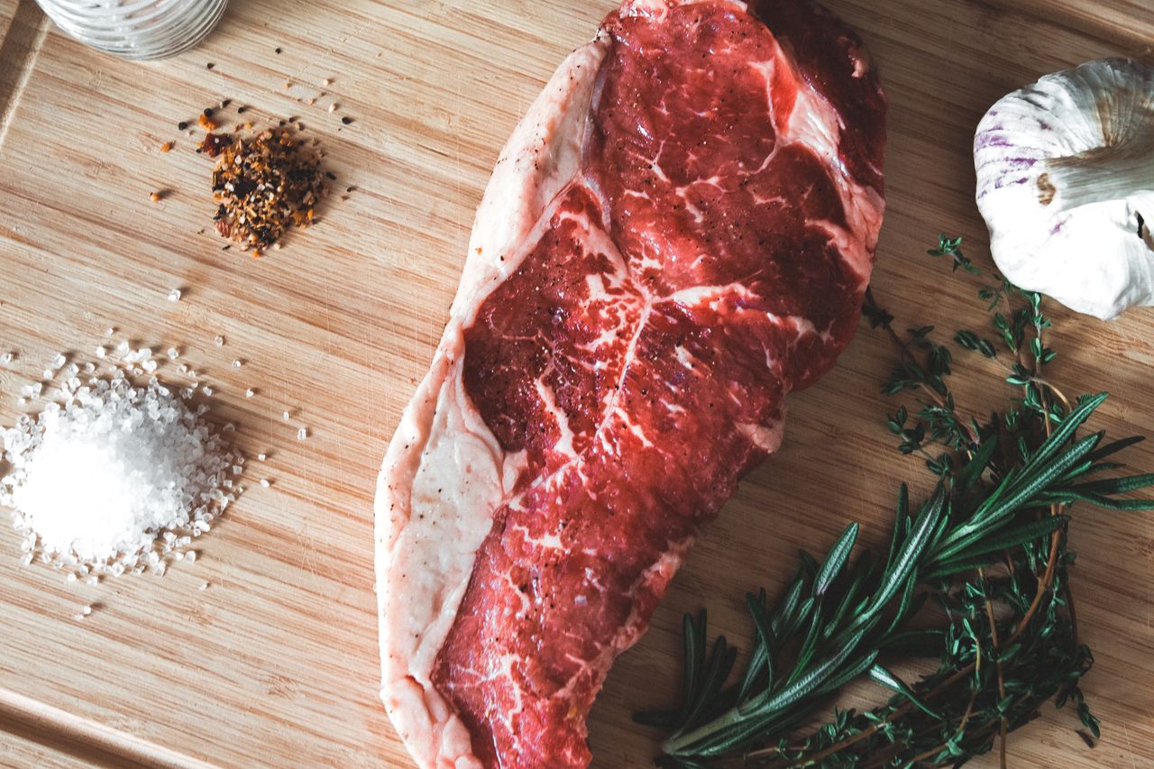 Discover raw beef steak with garlic, rosemary, and spices on a wooden board, perfect for culinary inspiration.